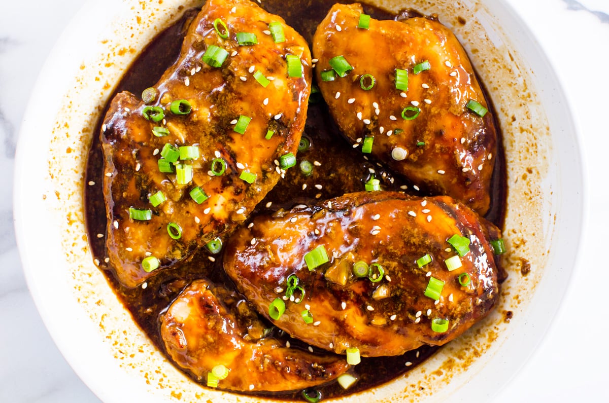 Four pieces of chicken in honey garlic sauce with green onion garnish. 